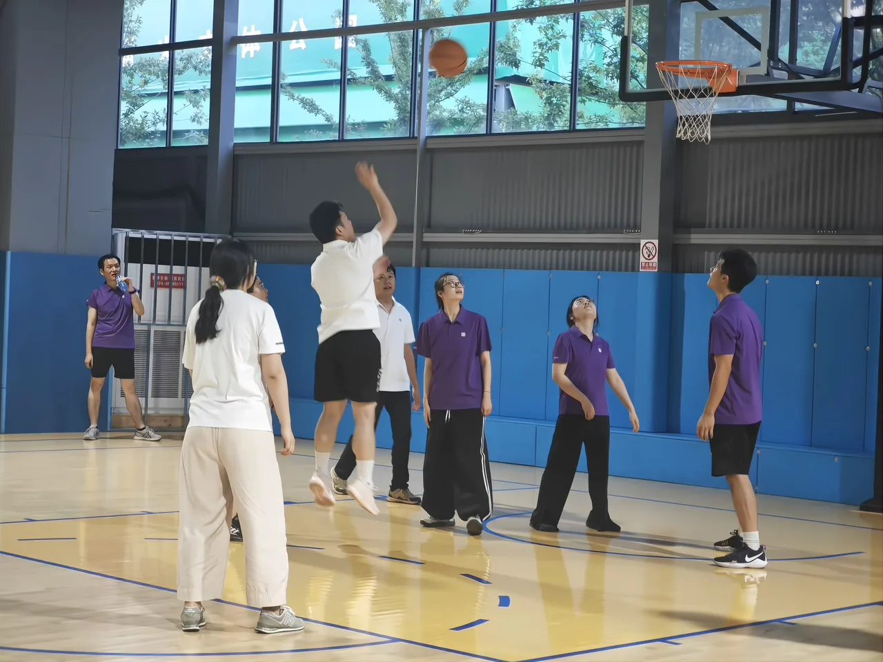 A colleague jumping to shoot in an indoor gym, the ball mid-flight toward the hoop, teammates watching